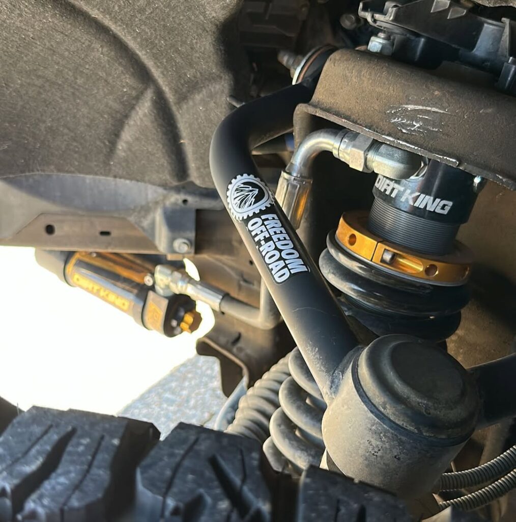 Close-up of Freedom Off-Road control arm paired with Dirt King coilovers on a modified off-road truck.